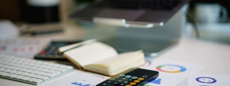 Calculatrice, documents financiers et stylo sur un bureau, pour comparer le coût d'une assistante administrative salariée et indépendante