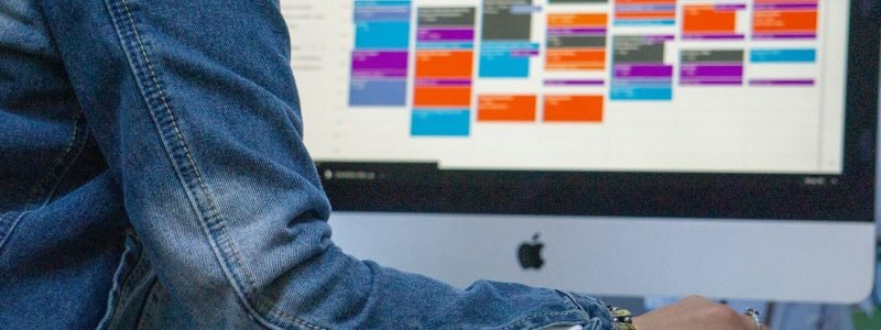 A person in a denim jacket using a computer with a colorful calendar display